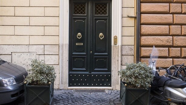 A black double door with a brass knocker, flanked by two potted plants, and a cobblestone pavement leading to it. - NAVONA PENTHOUSE APARTMENT WITH TERRACES (Roma)