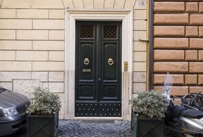 A black double door with a brass knocker, flanked by two potted plants, and a cobblestone pavement leading to it. - NAVONA PENTHOUSE APARTMENT WITH TERRACES (Roma)