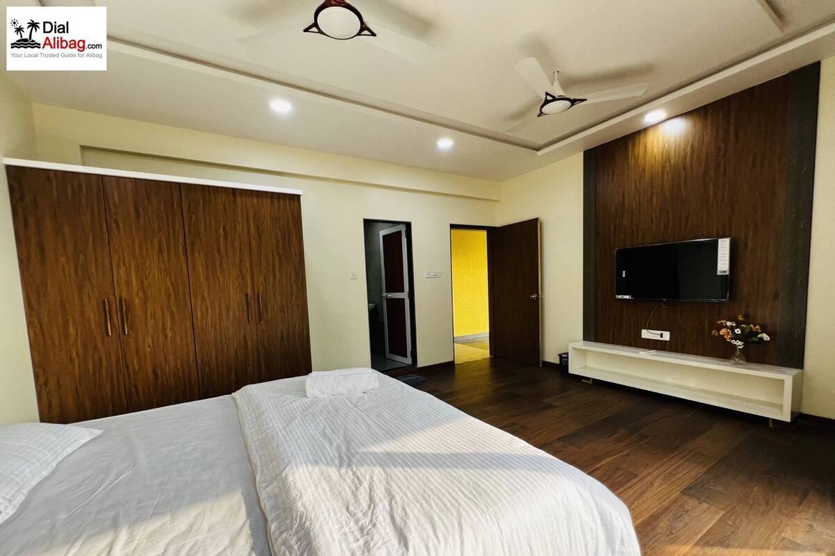 A hotel room with two beds, a TV, wooden wardrobe, and a bright hallway.