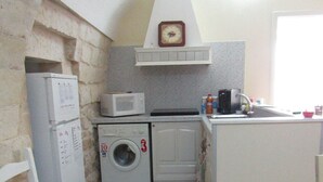 A compact kitchen with a washing machine, microwave, and a small sink. - The Courtyard Room Fishing (Scicli)