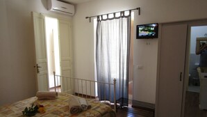 A bedroom with a bed, a TV mounted on the wall, and a bathroom visible through an open door. - The Courtyard Room Fishing (Scicli)