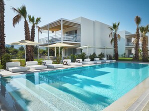 A modern pool area with white lounge chairs and umbrellas, surrounded by palm trees and a two-story building with balconies.