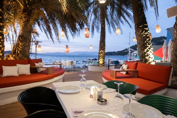 A restaurant with outdoor seating, palm trees, and a view of the sea. - Flamm Residences (Bodrum)