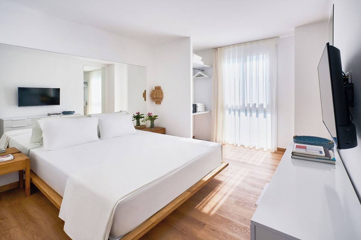 A modern hotel room with a large bed, a flat-screen TV, a bedside table with a lamp, and a wardrobe.