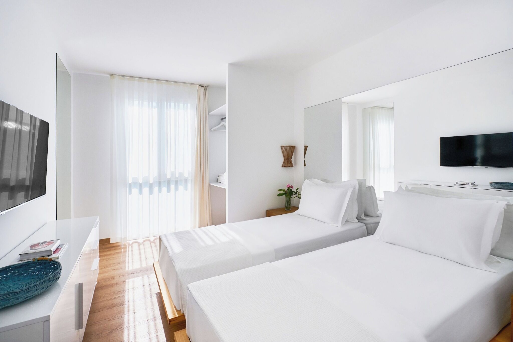 A hotel room with two beds, a TV, a desk, and a window with curtains.