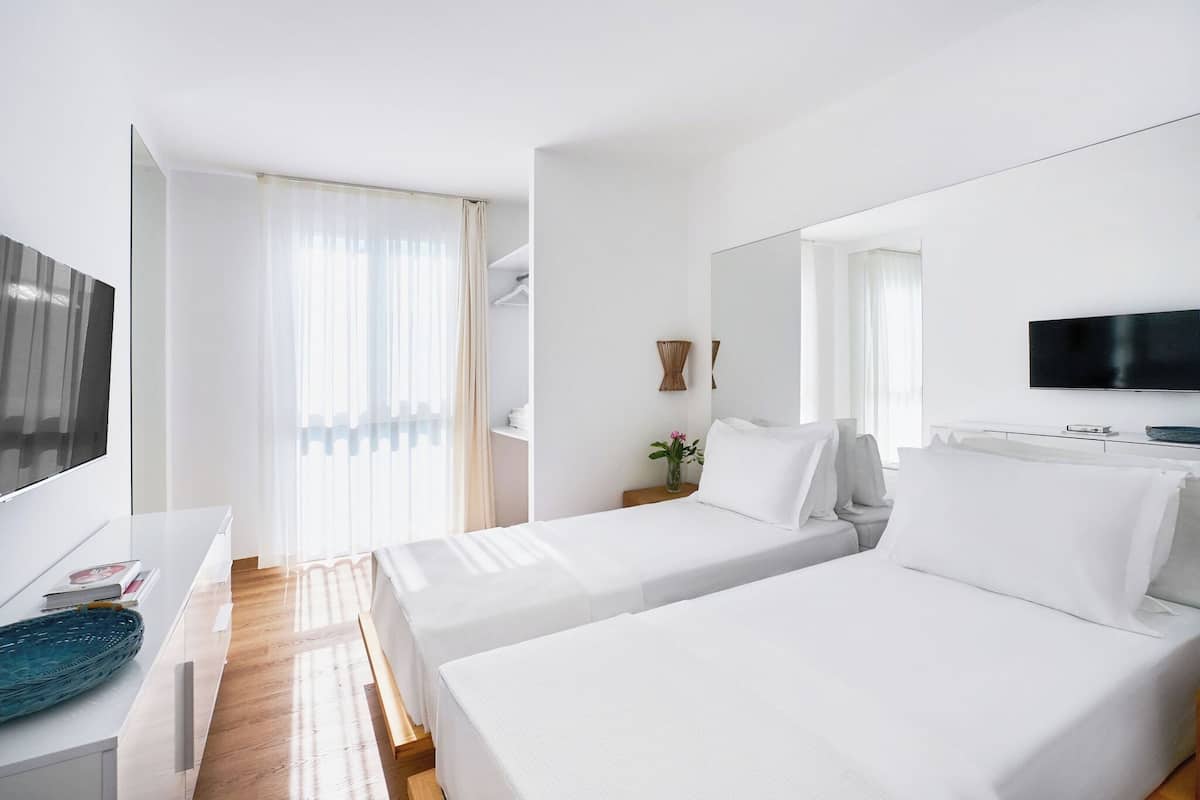 A hotel room with two beds, a TV, a desk, and a window with curtains.
