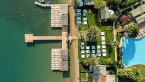 An aerial view of a resort with a wooden dock, multiple lounge areas with sunbeds, a swimming pool, and lush landscaping. - Flamm Residences (Bodrum)