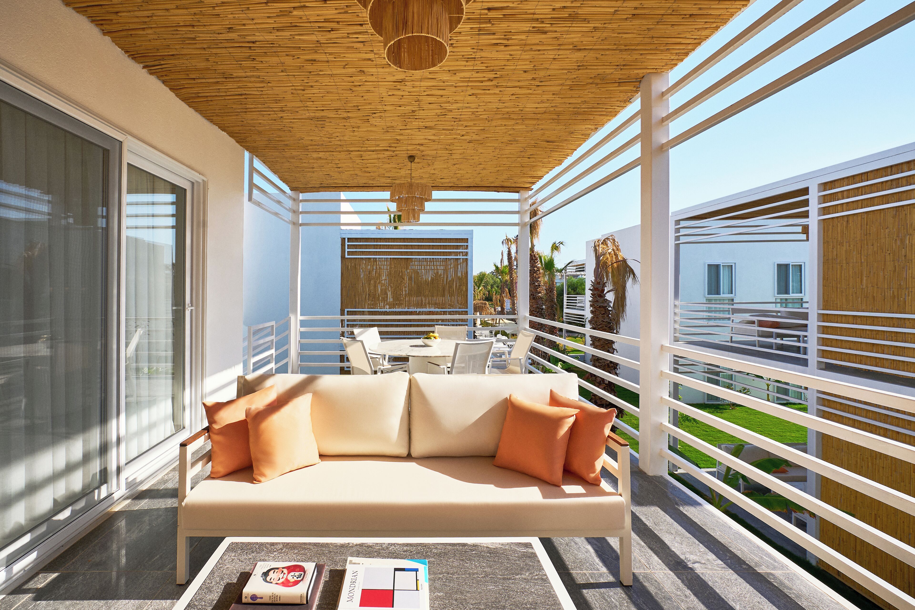 Un balcon moderne avec un canapé beige, une petite table avec des livres et une vue sur un jardin et des immeubles.