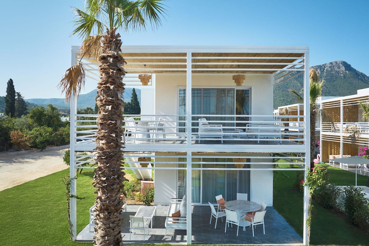 A modern two-story house with a balcony, outdoor seating, and a view of the mountains.