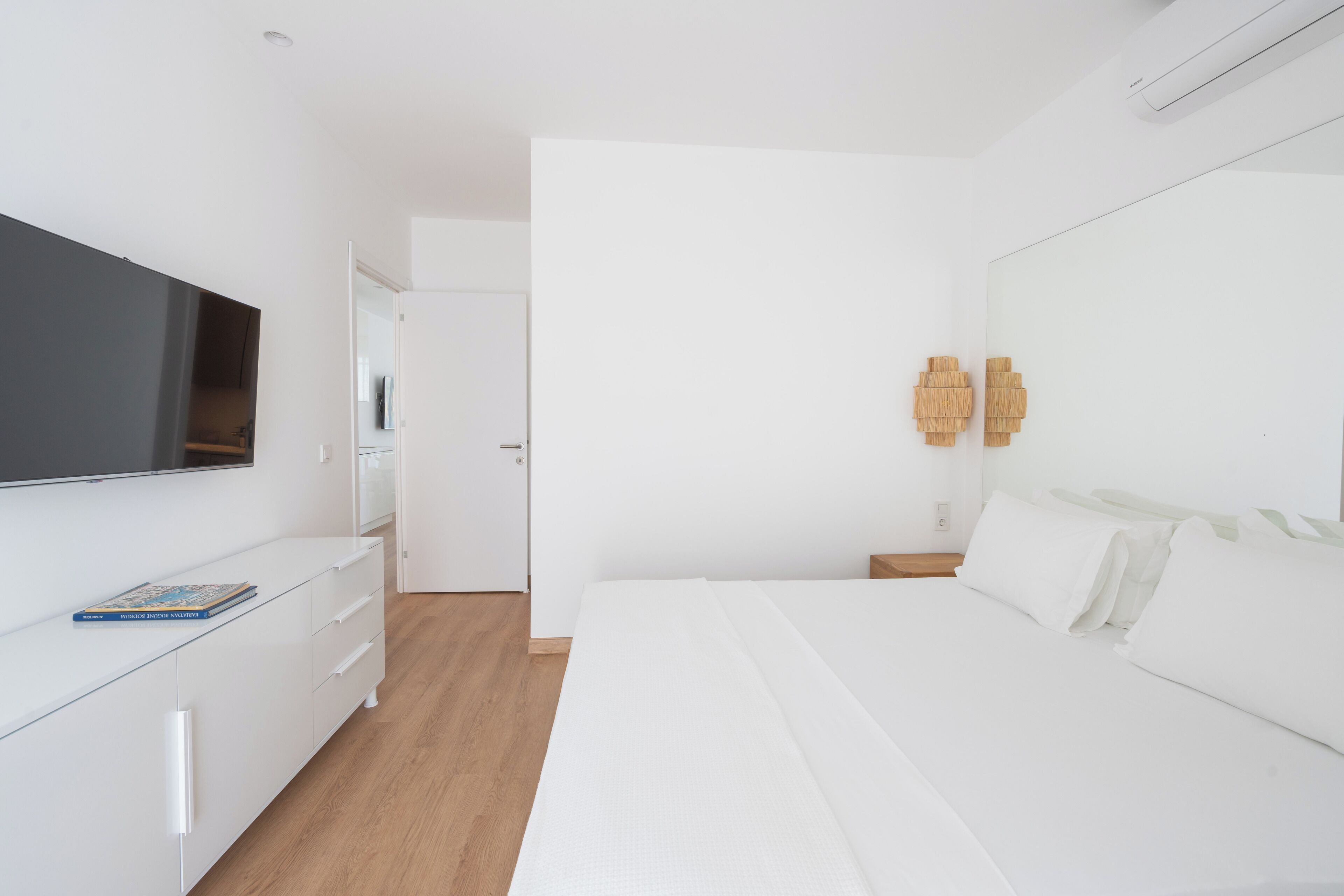 A modern bedroom with a large bed, a TV mounted on the wall, and a minimalist design.
