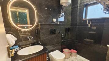 Een moderne badkamer met een zwart marmeren wastafelmeubel, een witte wastafel, een toilet en een douchehoek.