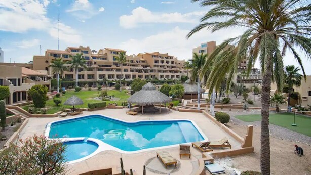 Un resort con piscina central, palmeras y un complejo de edificios al fondo.