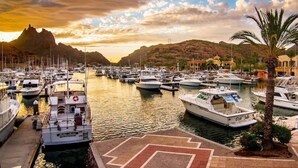Un puerto deportivo con numerosas embarcaciones amarradas, un telón de fondo montañoso y cielo despejado.