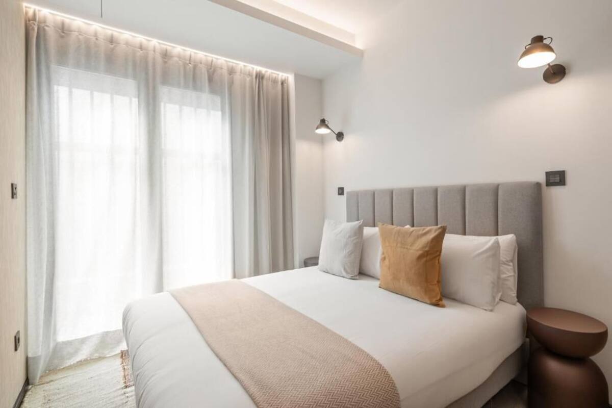 A modern hotel room with a large bed, a bedside table, and a window with curtains.