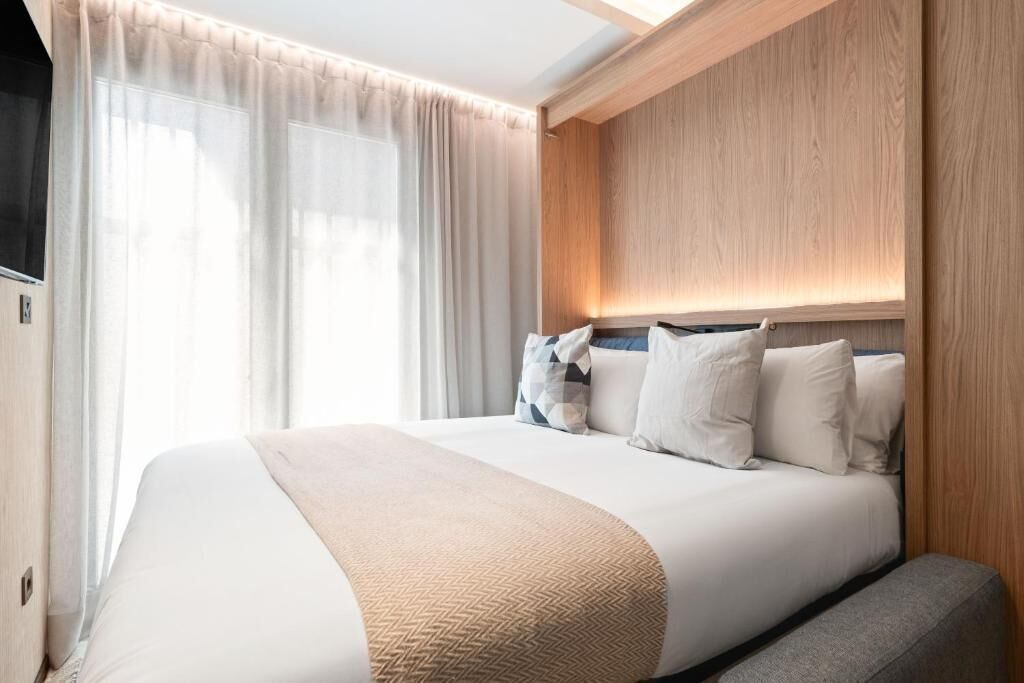 Une chambre d’hôtel avec un grand lit, une tête de lit en bois et une fenêtre ornée de rideaux légers.