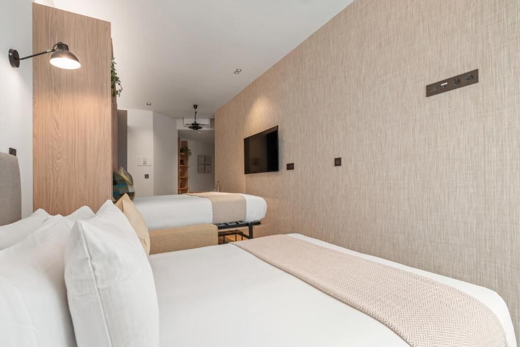 Moderni hotellihuone, jossa on suuri sänky, pienempi sänky, työpöytä ja seinälle asennettu televisio.