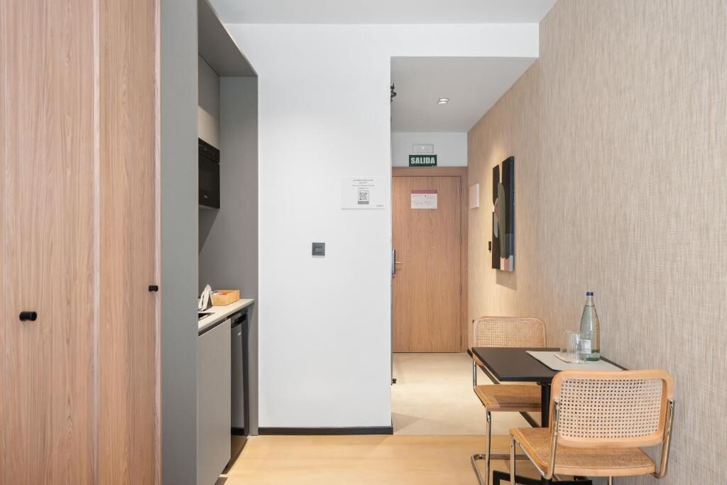 Un pasillo con una puerta de madera, una kitchenette, una mesa con sillas y un letrero que dice 'SALIDA'.