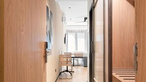 A hotel corridor with wooden walls, a seating area with a chair and table, and a view of a room with a bed and curtains. - Dobo Madrid Moncayo (Madrid)