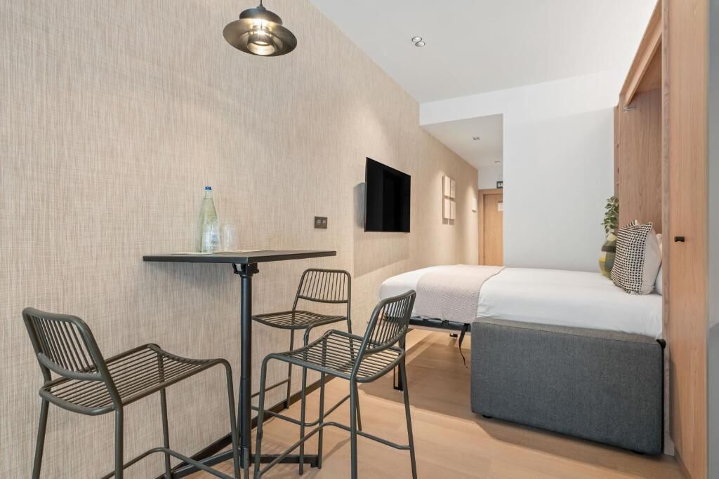 Una habitación de hotel moderna con una cama, una mesita y dos sillas.