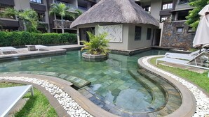 Ein Swimmingpool mit Liegestühlen und einer strohgedeckten Struktur.