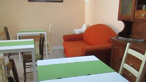 A dining area with tables and chairs, a sofa, and a cabinet. - The Red Room Courtyard (Scicli)