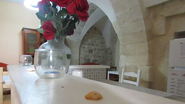 A dining area with a white table, a vase with red roses, a glass, and a small pastry on the table. - The Red Room Courtyard (Scicli)