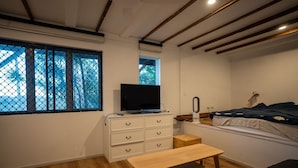 A bedroom with a bed, a TV on a dresser, a window with a view, and a wooden bench.