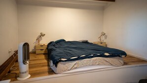 A bedroom with a bed, bedside lamps, a heater, and a wooden floor.