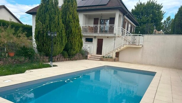 A rectangular swimming pool with a tiled deck, surrounded by a low wall and a house with a balcony. - Les Bords de la Lizaine (Hericourt)