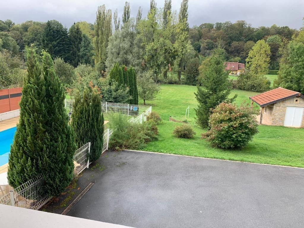 Een woonhuis met omheinde tuin, zwembad en uitzicht op een groen landschap met bomen en een gebouw in de verte.