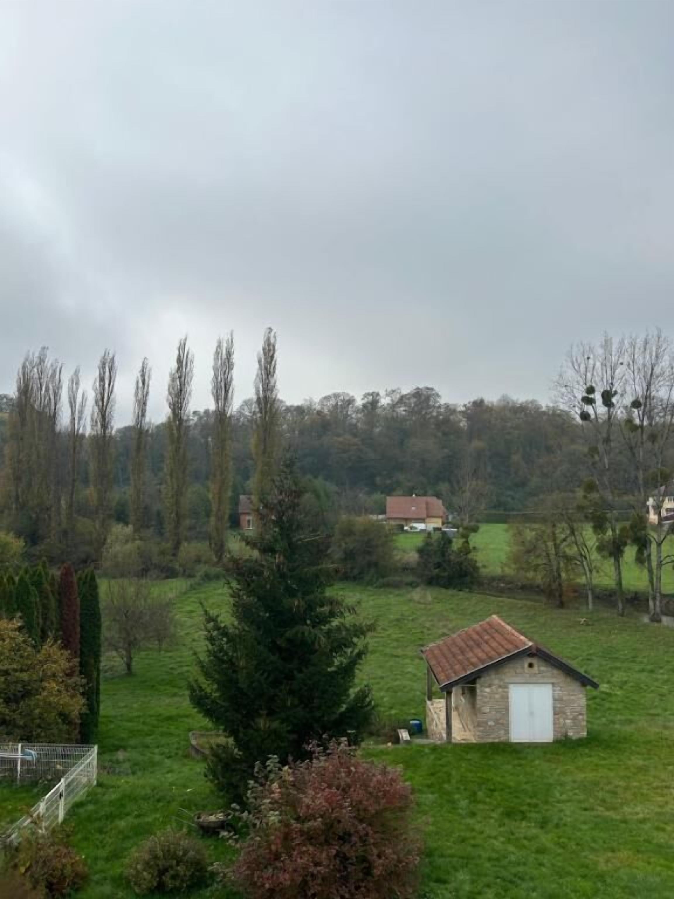 A rural landscape with a stone building, a fenced area, and a variety of trees.