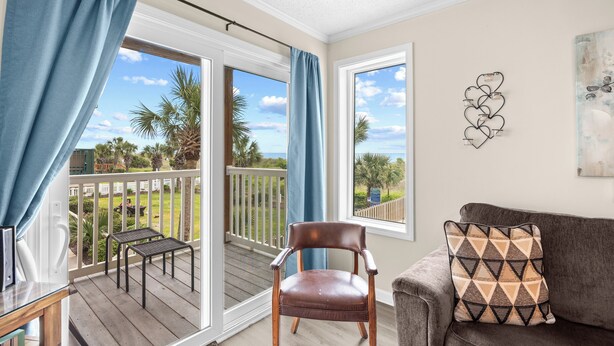 A room with a balcony, a leather chair, a sofa, and a wall art piece. - Dog Friendly-Windy Village-Oceanfront-Sleeps6-2br/2ba-Full Kitchen-Free Parking (North Myrtle Beach)