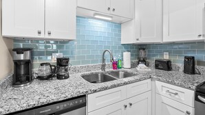 A kitchen with white cabinets, a granite countertop, a double sink, and various appliances including a coffee maker, toaster, and blender. - Dog Friendly-Windy Village-Oceanfront-Sleeps6-2br/2ba-Full Kitchen-Free Parking (North Myrtle Beach)