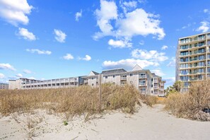 A beachfront hotel with multiple floors, a sandy path leading to the entrance, and a clear sky. - Windy Village Getaway-Oceanfront-Sleep6-2br/2ba-Full Kitchen-Pool-Free Parking (North Myrtle Beach)