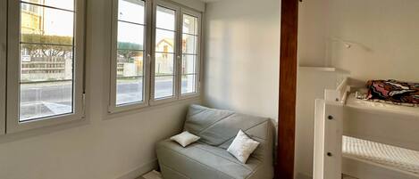A room with a grey sofa, a striped rug, and a window with a view of a street and buildings.