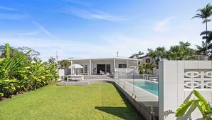 Ett modernt hus med en swimmingpool, en täckt uteplats och en välskött gräsmatta.
