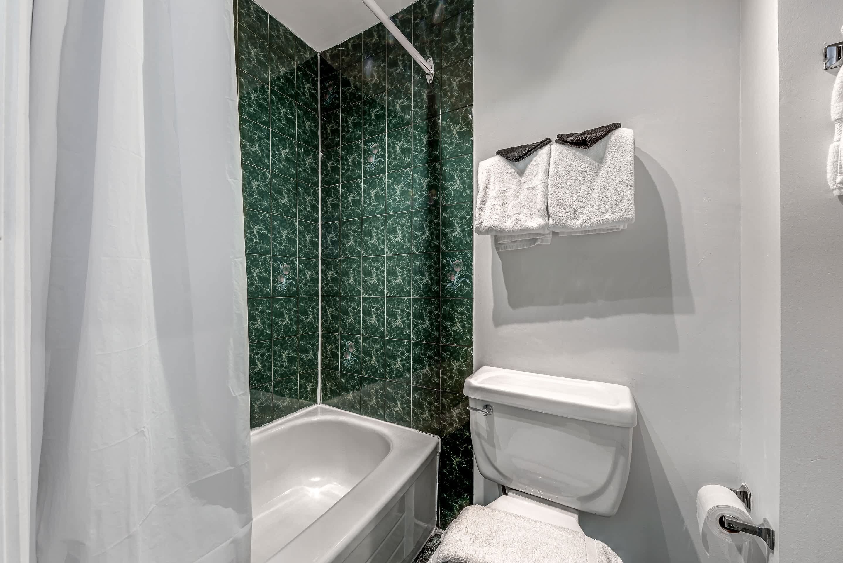 Un baño con bañera, inodoro y azulejos de mármol verde.