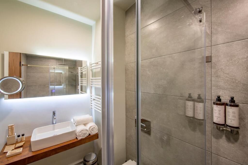 A modern bathroom with a glass shower enclosure, a vanity with a sink and towel rack, and toiletries on the wall.