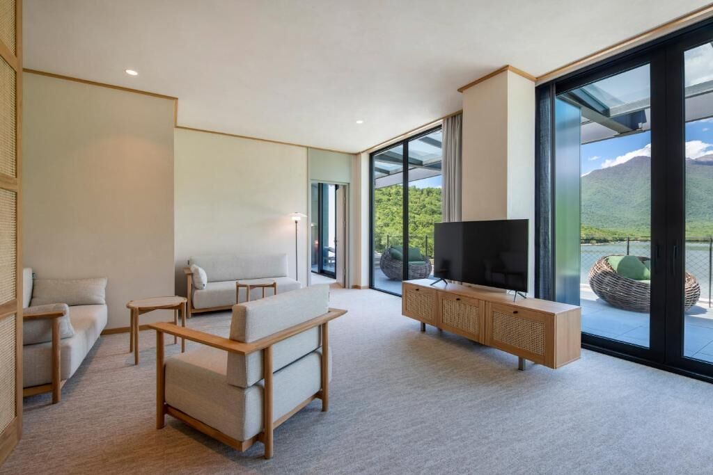 A modern living room with a large TV, comfortable seating, and a view of mountains through large glass doors.
