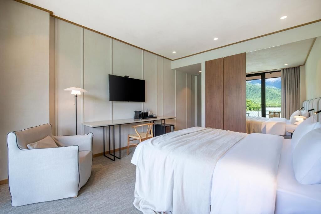 Habitación de hotel moderna con una cama grande, un escritorio con televisor de pantalla plana, una silla y vistas al exterior.