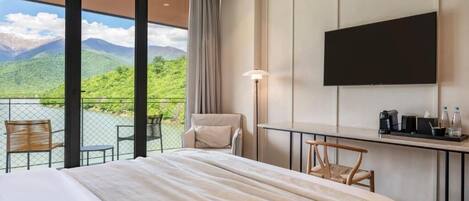 A hotel room with a large bed, a desk, a chair, a TV, and a balcony with a mountain view.