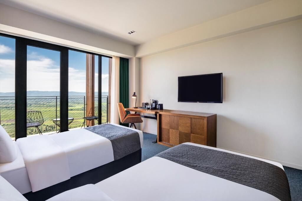 Habitación de hotel con dos camas, un escritorio, una silla y una televisión.