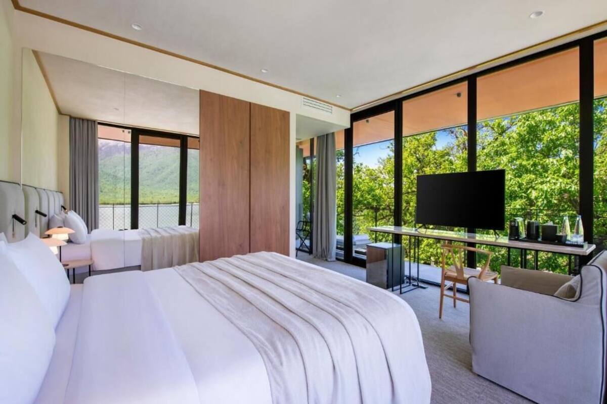 A modern hotel room with a large bed, a desk with a TV, and a balcony with a scenic view.