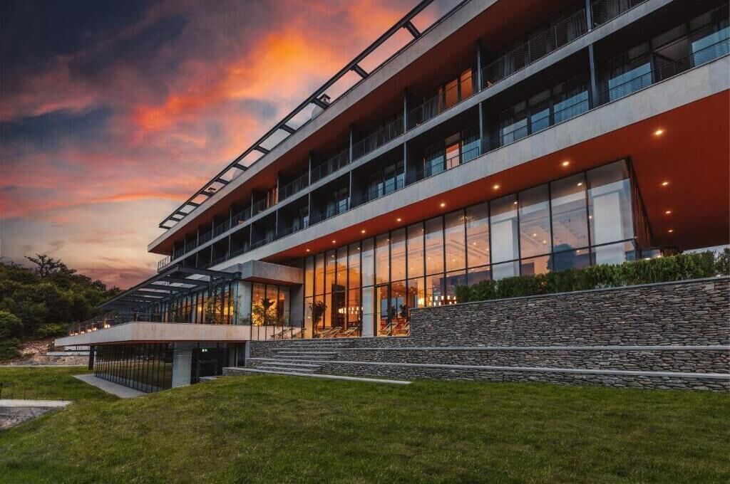Un bâtiment moderne doté d’une façade en verre, de plusieurs étages et d’un mur de soutènement en pierre.