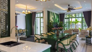 A modern dining area with a glass table, green chairs, and a kitchen with a sink. - Fortune Villa Phu Quoc (An Thoi)