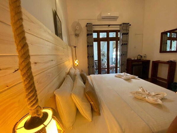 A hotel room with a large bed, a headboard, a bedside table, a lamp, a window with curtains, and an air conditioning unit. - ella dream mount (Ella)