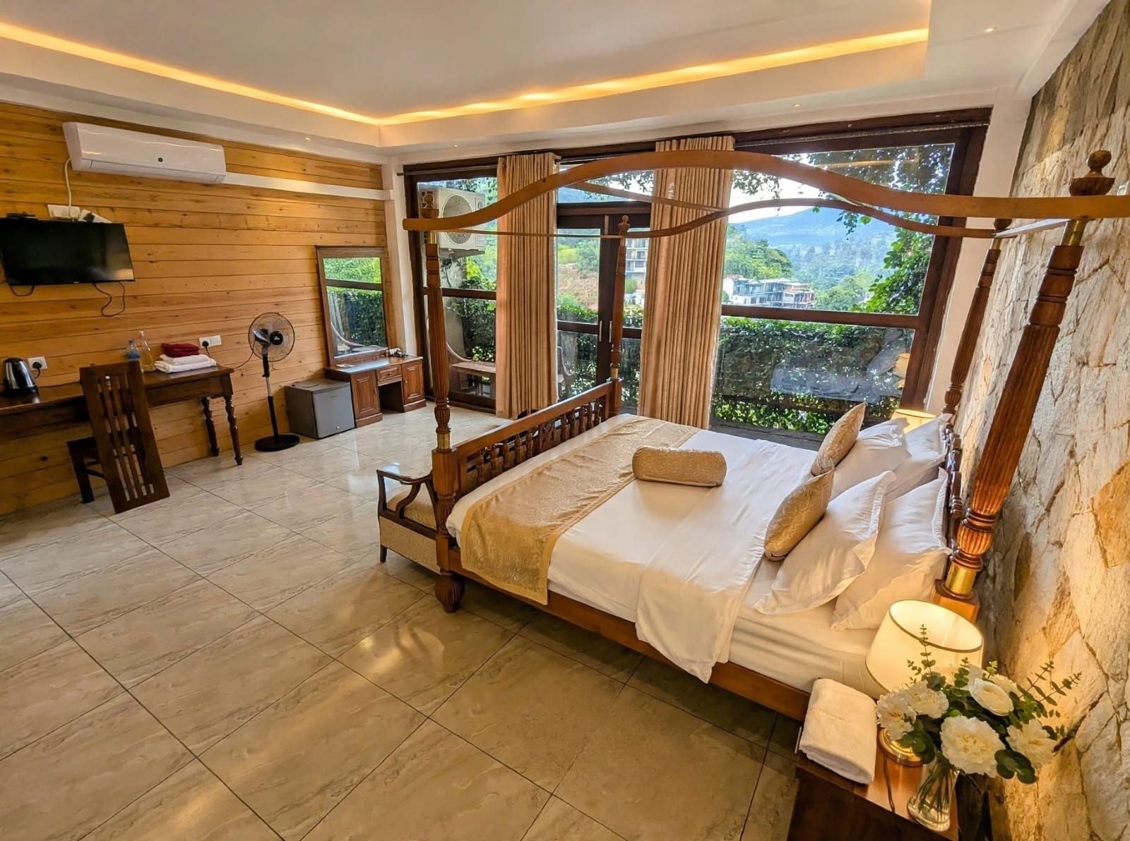 A four-poster bed with a canopy, a desk with a chair, a television, and a large window with curtains.