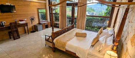 A four-poster bed with a canopy, a desk with a chair, a television, and a large window with curtains.