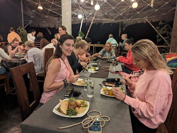 A group of people dining at an outdoor restaurant with a thatched roof and hanging lights. - ella dream mount (Ella)