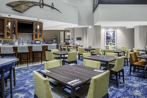 A hotel dining area with multiple tables and chairs, a bar area with a counter and bar stools, and a view of the outdoors through a window. - Near Ravenel Bridge | Pool. Bar & Dining (Mount Pleasant,  Charleston,)